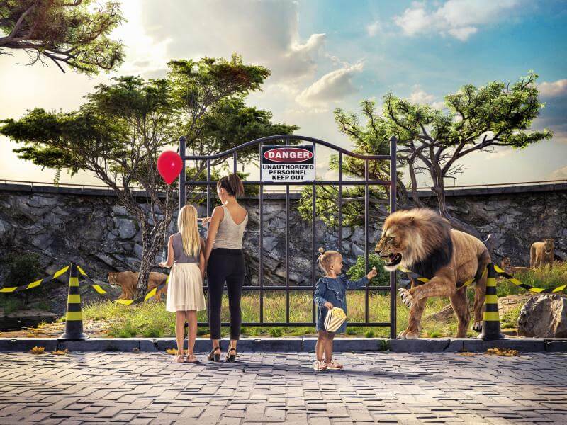 A mother and two children standing at a fence so poor it doesn't protect against a lion coming out.